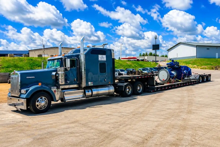 Heavy haul truck transporting large industrial equipment secured on a lowboy trailer in a loading yard