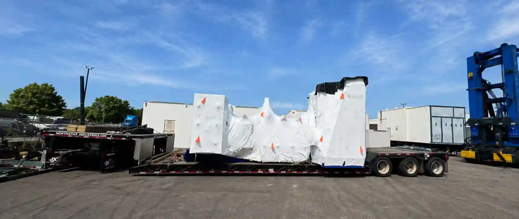 Flatbed trailer transporting oversized industrial equipment wrapped in protective covering for heavy haul delivery