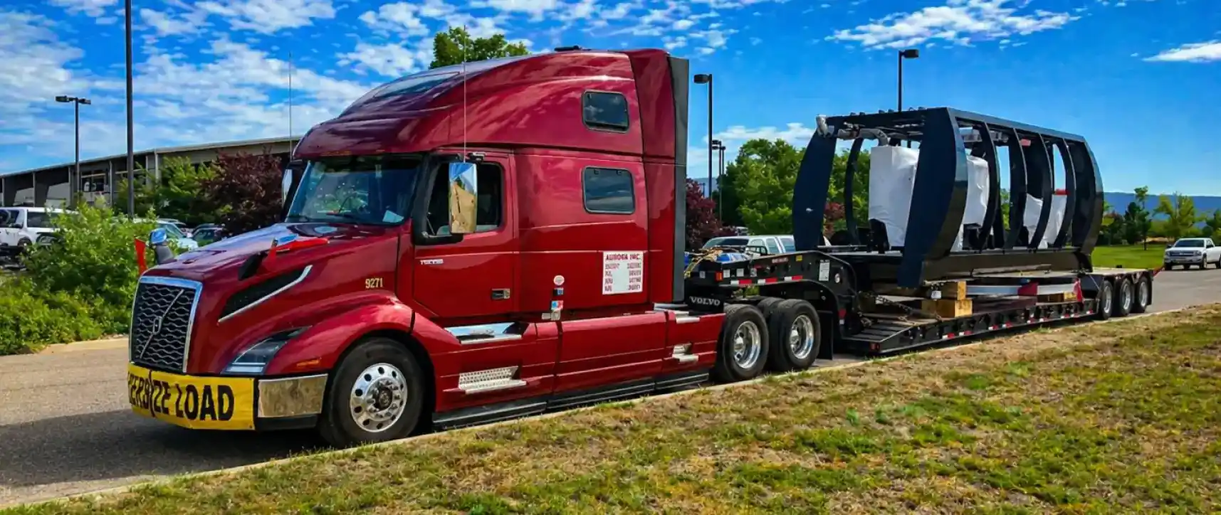 Red semi truck hauling oversized specialized industrial frame structure on a flatbed trailer with oversize load sign