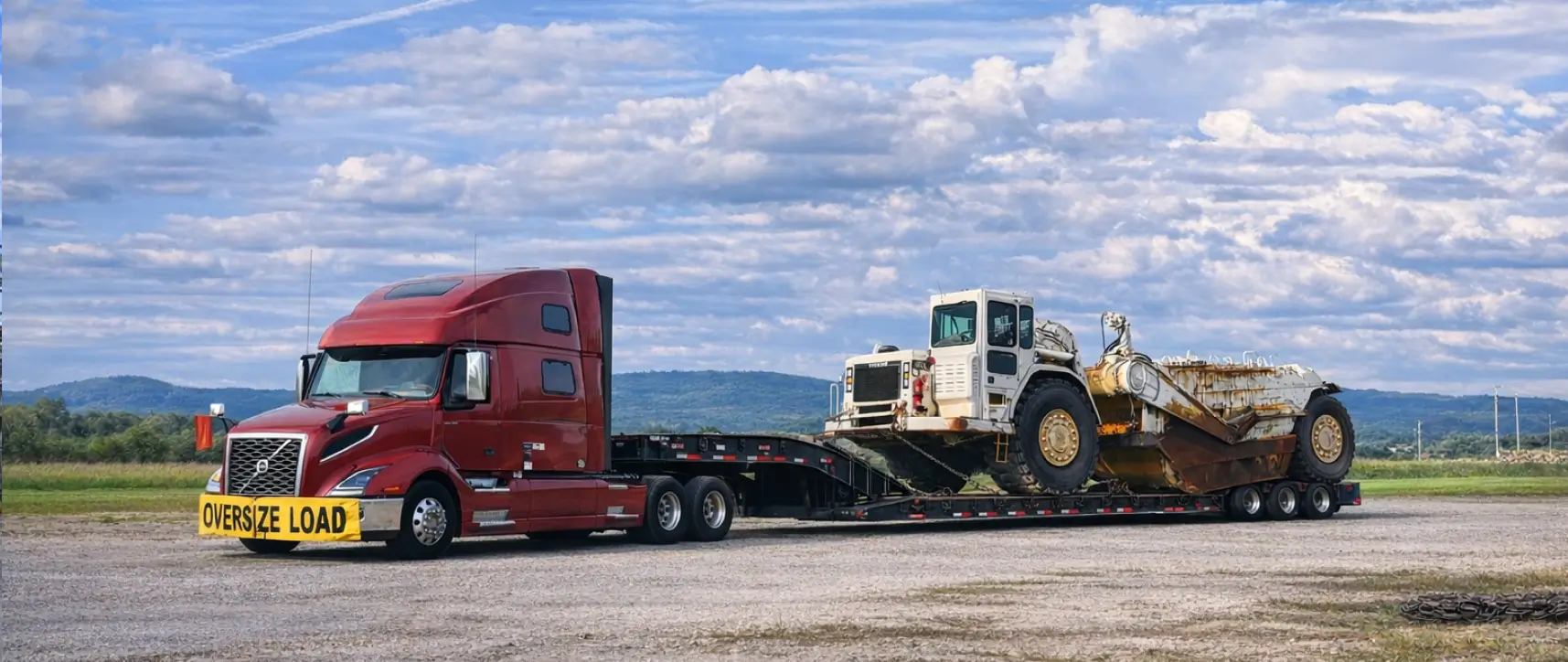 Oversize mining scraper transported on a lowboy trailer by a heavy haul truck