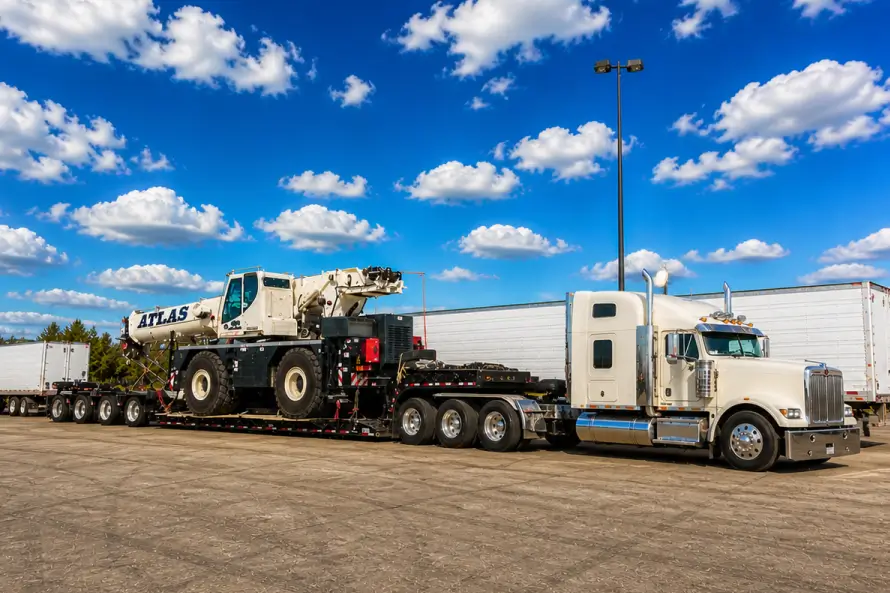 Heavy haul truck transporting a large mobile crane on a multi axle lowboy trailer in an industrial yard
