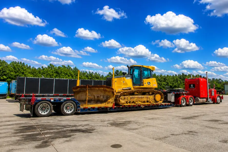 Heavy haul truck transporting a bulldozer on a lowboy trailer at an industrial site