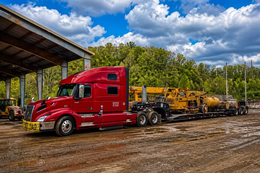 Heavy haul truck transporting large industrial machinery on a lowboy trailer at a construction yard