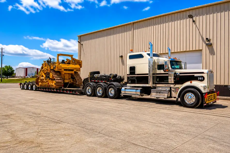 Heavy haul truck transporting a large crawler dozer on a lowboy trailer at an industrial facility