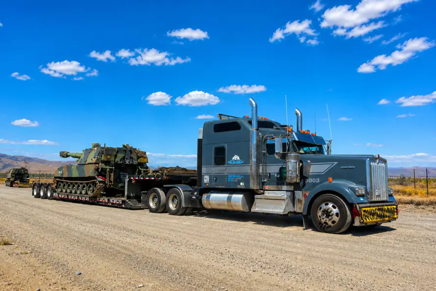 Tanque militar sobredimensionado transportado en un remolque de plataforma por un camión de carga pesada en una carretera desértica