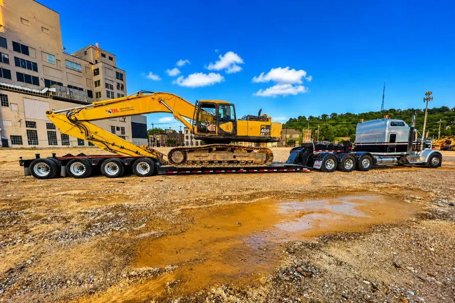 Camión de carga pesada transportando una gran excavadora en un remolque lowboy en una zona urbana de construcción
