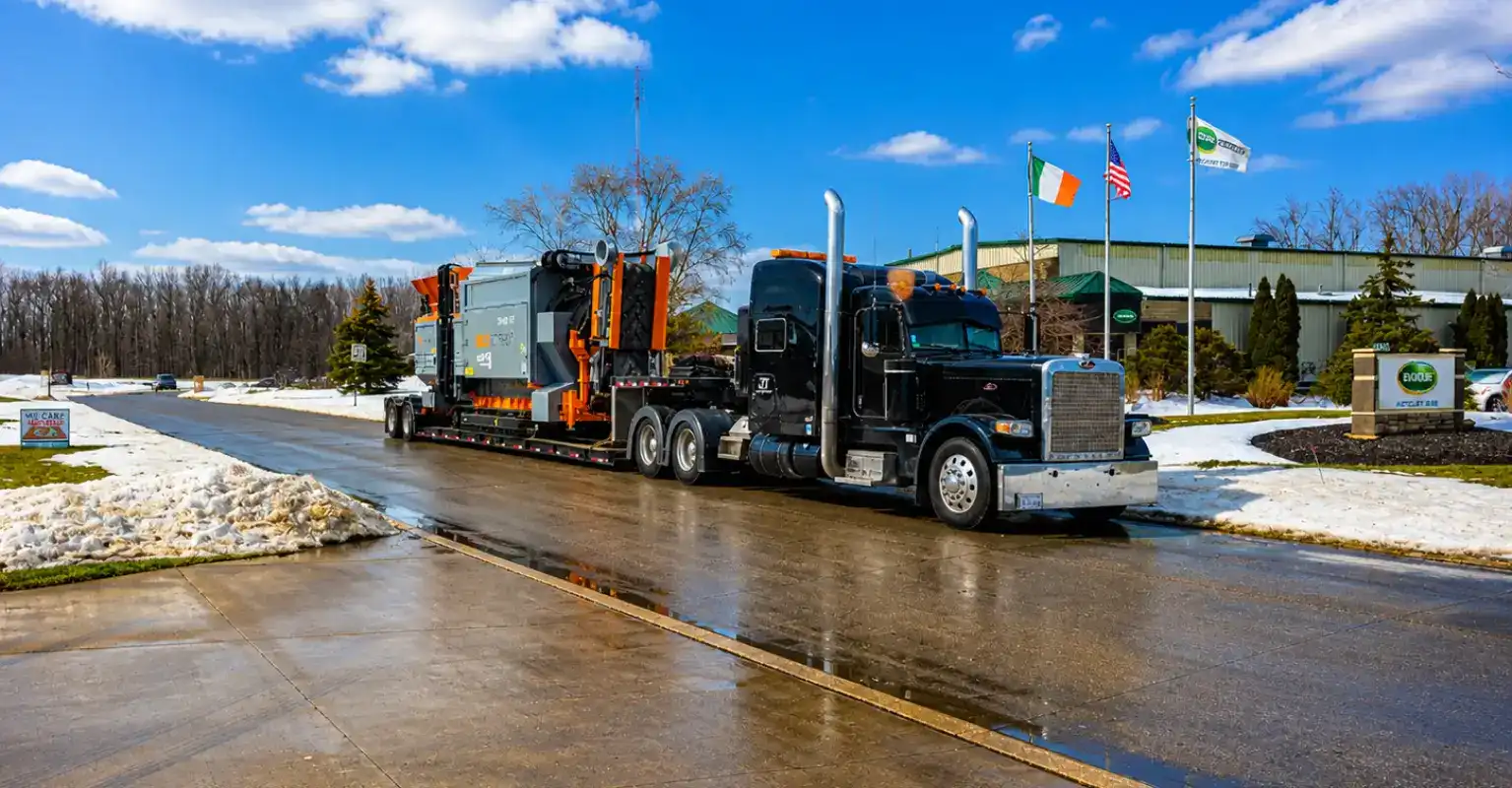 Equipo industrial sobredimensionado transportado en un remolque lowboy por un camión de carga pesada en una carretera mojada de invierno cerca de una instalación industrial