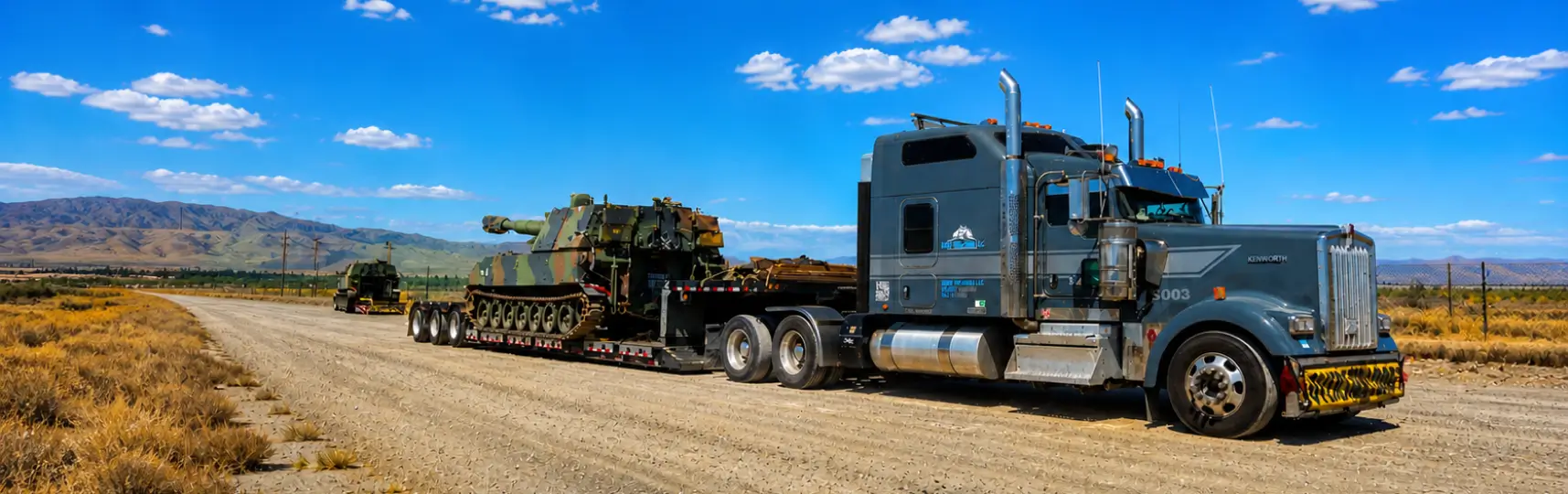Oversize military tank transported on a flatbed trailer by a heavy haul truck on a desert road
