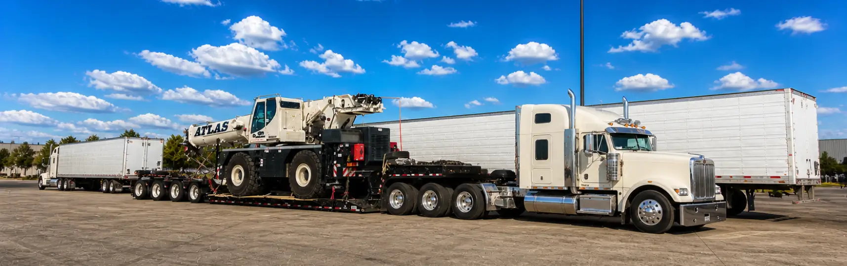 Heavy haul truck transporting a large mobile crane on a multi axle lowboy trailer in an industrial yard
