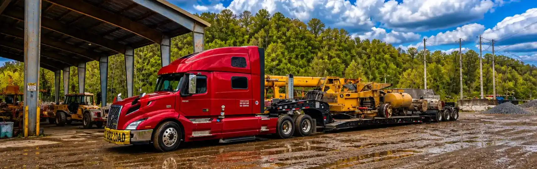 Camión de carga pesada transportando maquinaria industrial grande en un remolque lowboy en un patio de construcción